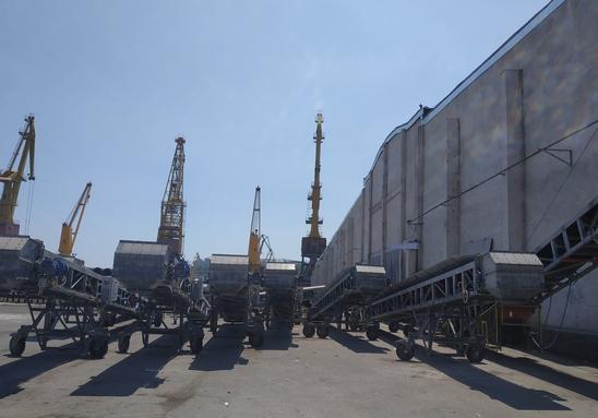 Un rând de benzi transportoare mobile pe roți, amplasate într-o zonă deschisă a terminalului portuar