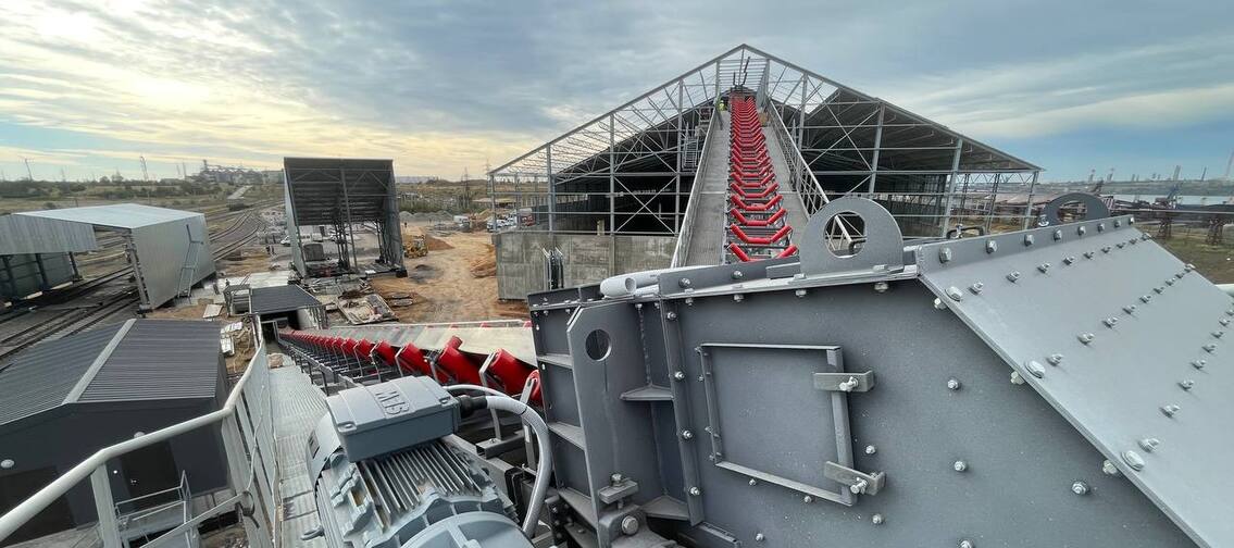 Привідна станція стрічкового конвеєра з двигуном на передньому плані та видом на похилу галерею і склад підлогового зберігання