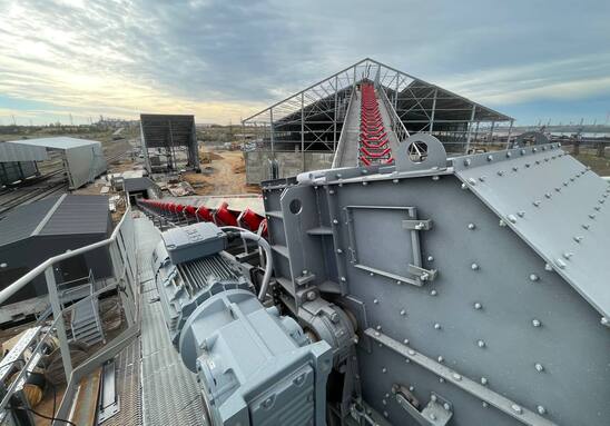 Stația de acționare a transportorului cu bandă cu motor în prim-plan, oferind o vedere asupra galeriei înclinate și a depozitului de stocare pe pardoseală