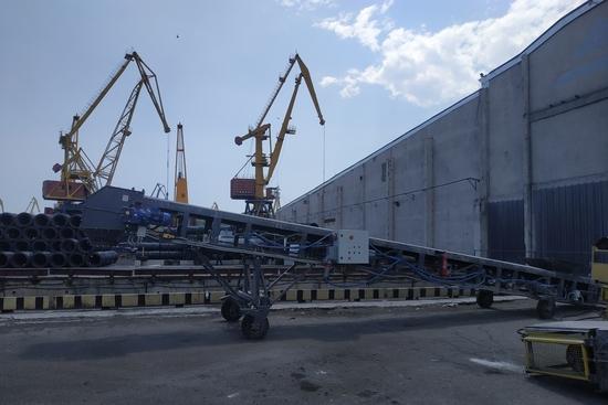 Окремий мобільний стрічковий конвеєр з електроприводом та щитом керування на тлі портових кранів